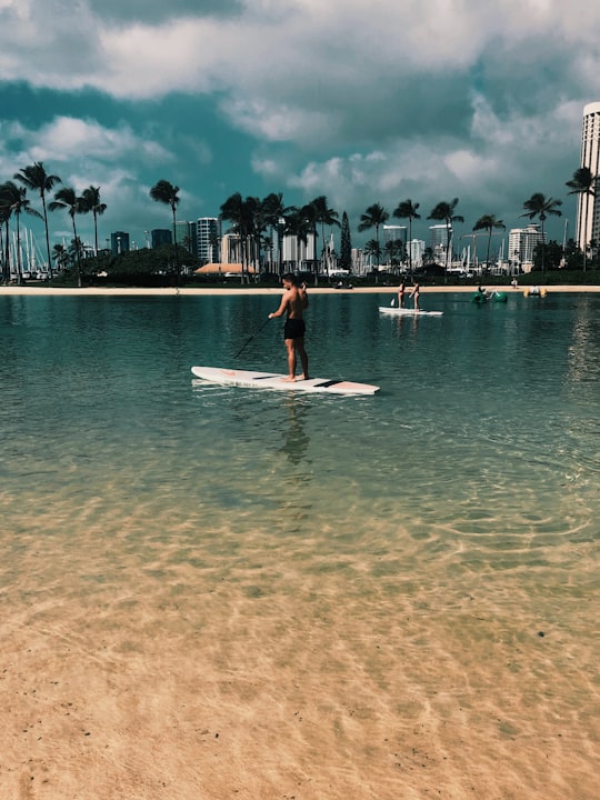 woman in red dress standing on white surfboard on beach during daytime in Duke Paoa Kahanamoku Lagoon United States