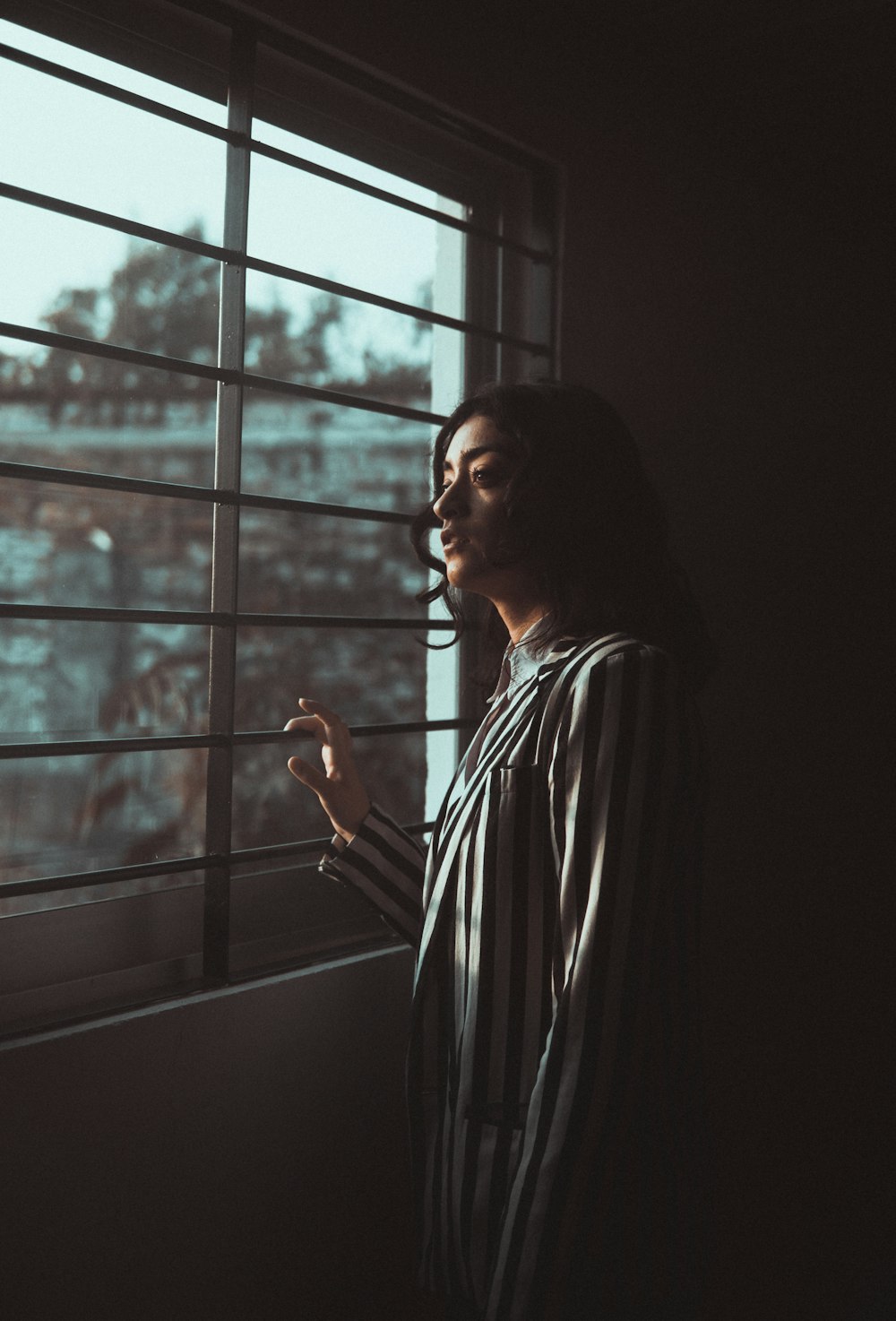 femme en chemise à manches longues rayée noire et blanche debout près de la fenêtre