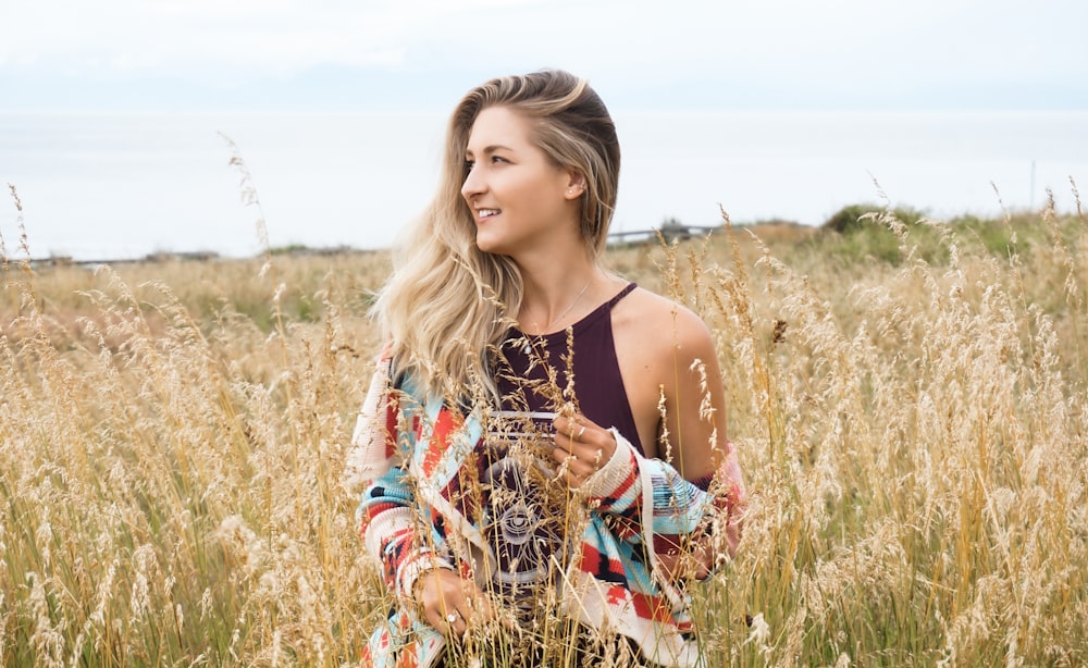 woman in black and brown floral spaghetti strap dress sitting on brown grass field during daytime