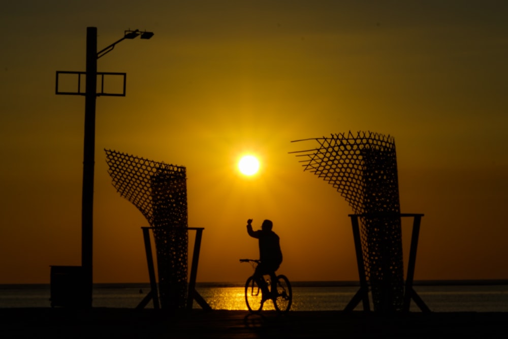 silhueta do homem que monta a bicicleta durante o pôr do sol