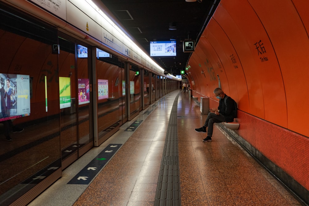 Mann in schwarzer Jacke sitzt auf Bahnhof