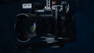 Cinematic close-up of a professional videographer adjusting a camera lens against a dark, moody backdrop.