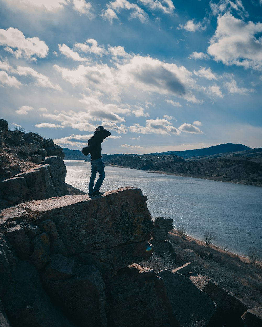 man in black jacket standing on rock near body of water during daytime