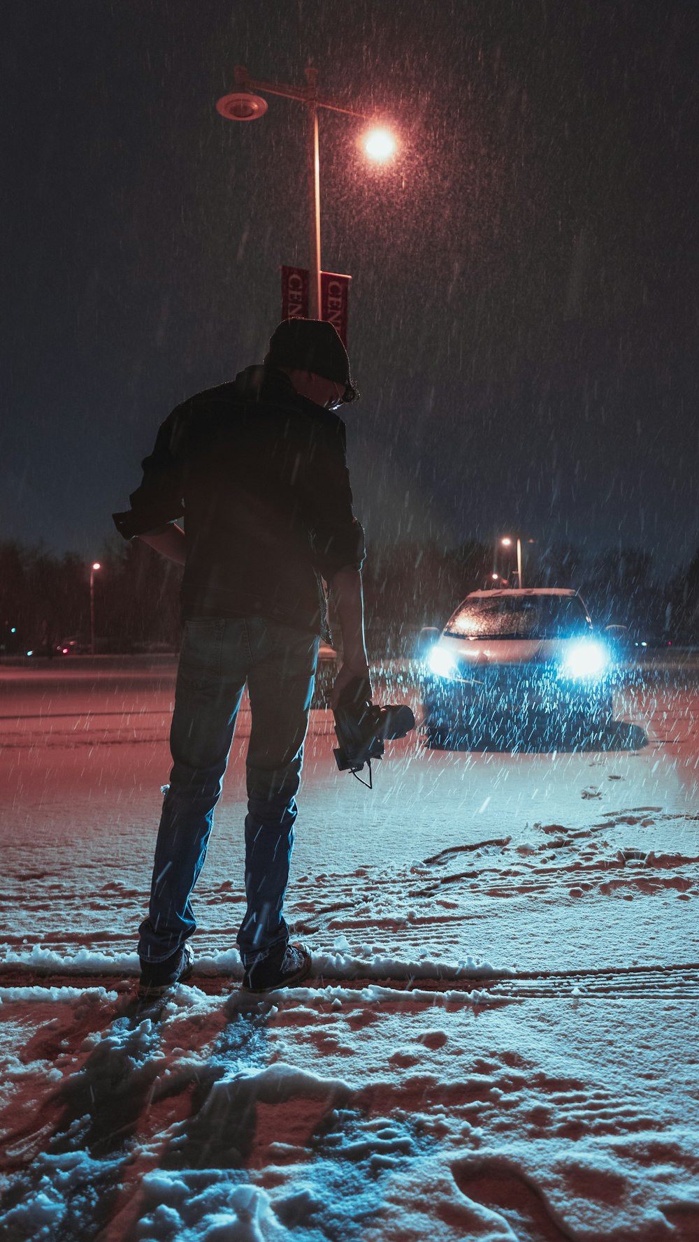 person in black jacket and blue denim jeans standing on snow covered ground during night time