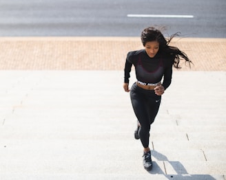 woman in black long sleeve shirt and black pants running on gray concrete road during daytime