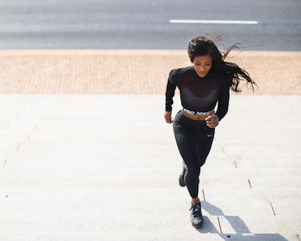 woman in black long sleeve shirt and black pants running on gray concrete road during daytime