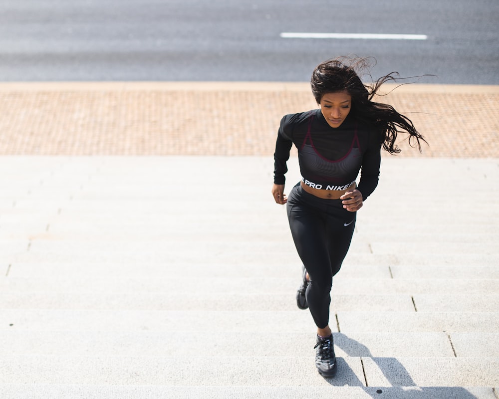 Donna in camicia nera a maniche lunghe e pantaloni neri che corre sulla strada di cemento grigia durante il giorno