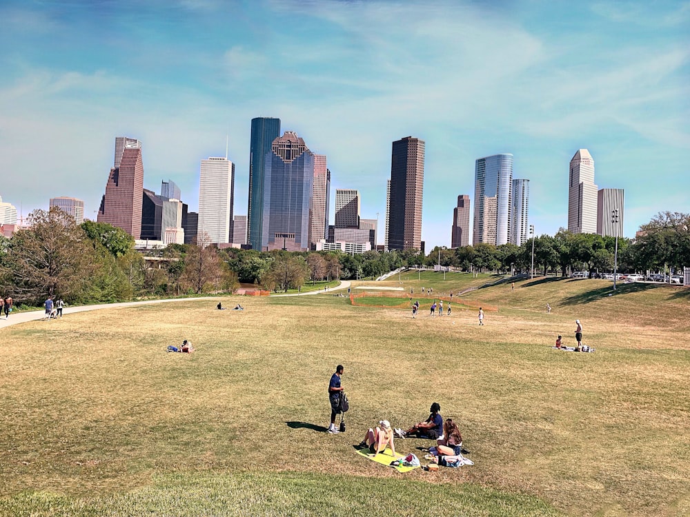 people sitting on green grass field near city buildings during daytime
