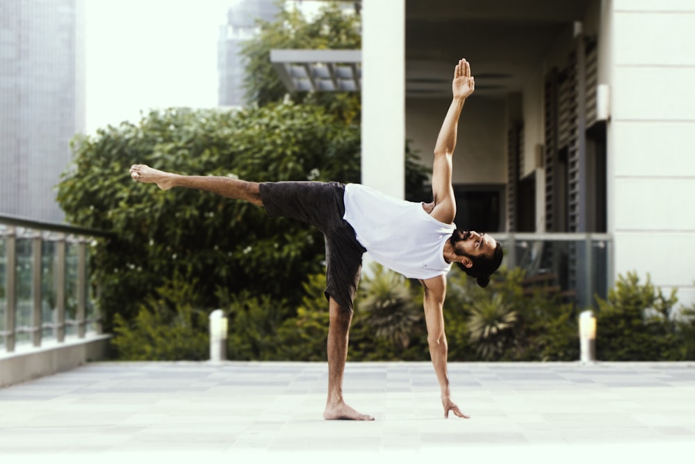 man in white tank top and black shorts doing yoga