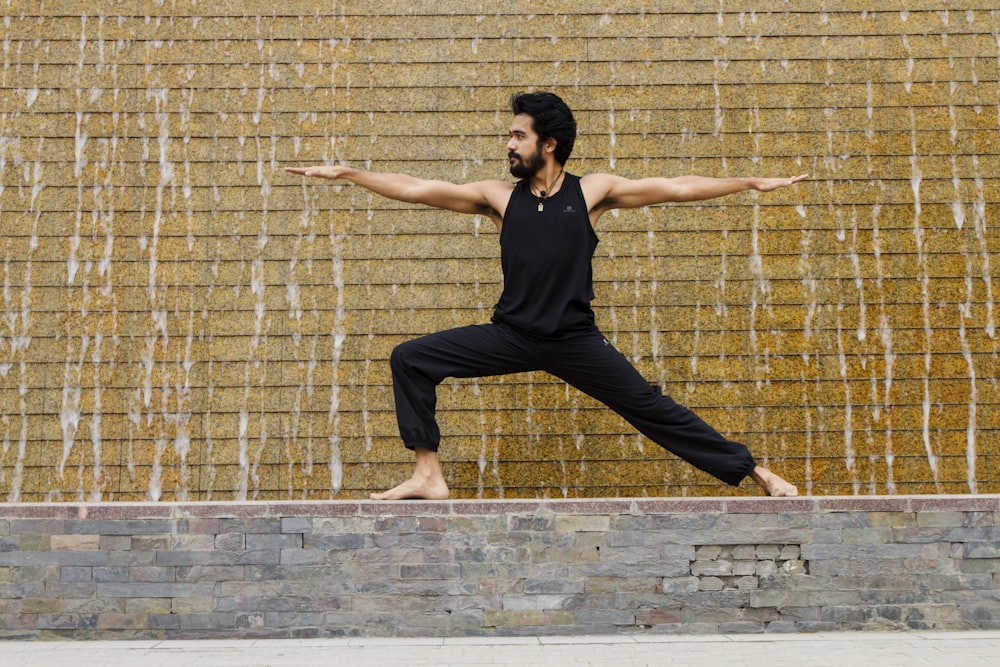 man in black tank top and black pants jumping on brown brick wall during daytime