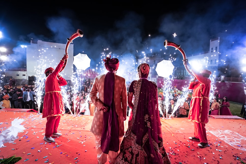 man and woman in red traditional dress dancing on brown sand during nighttime