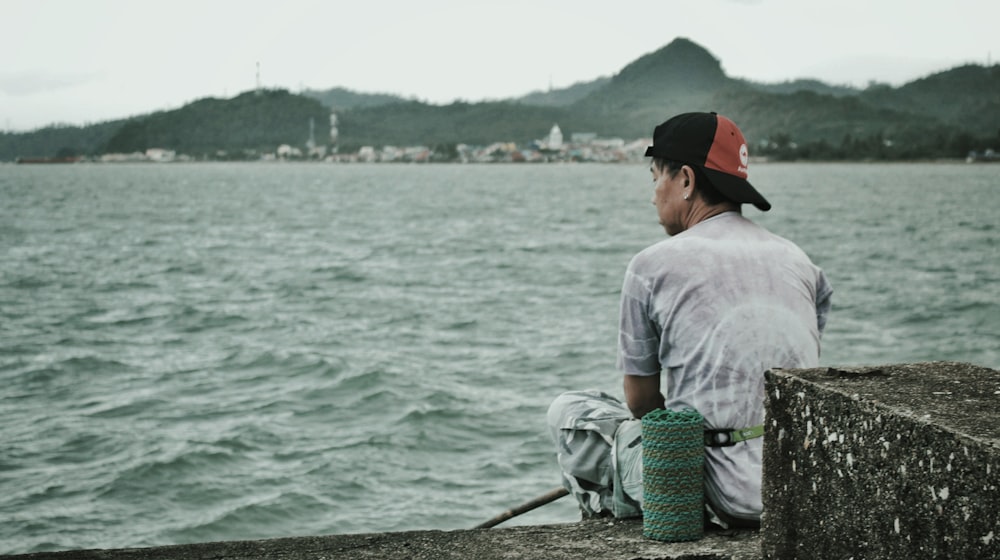 man in white shirt sitting on green net near body of water during daytime