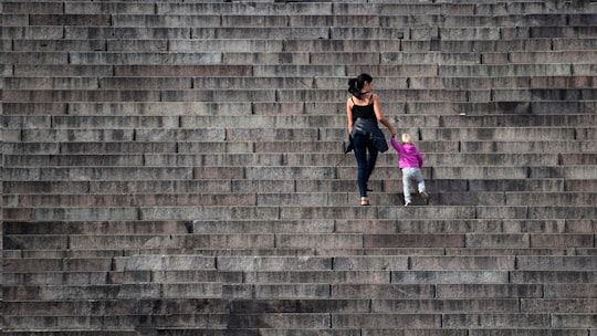 woman in purple tank top and blue denim jeans sitting on brown concrete stairs in Helsinki Cathedral Finland