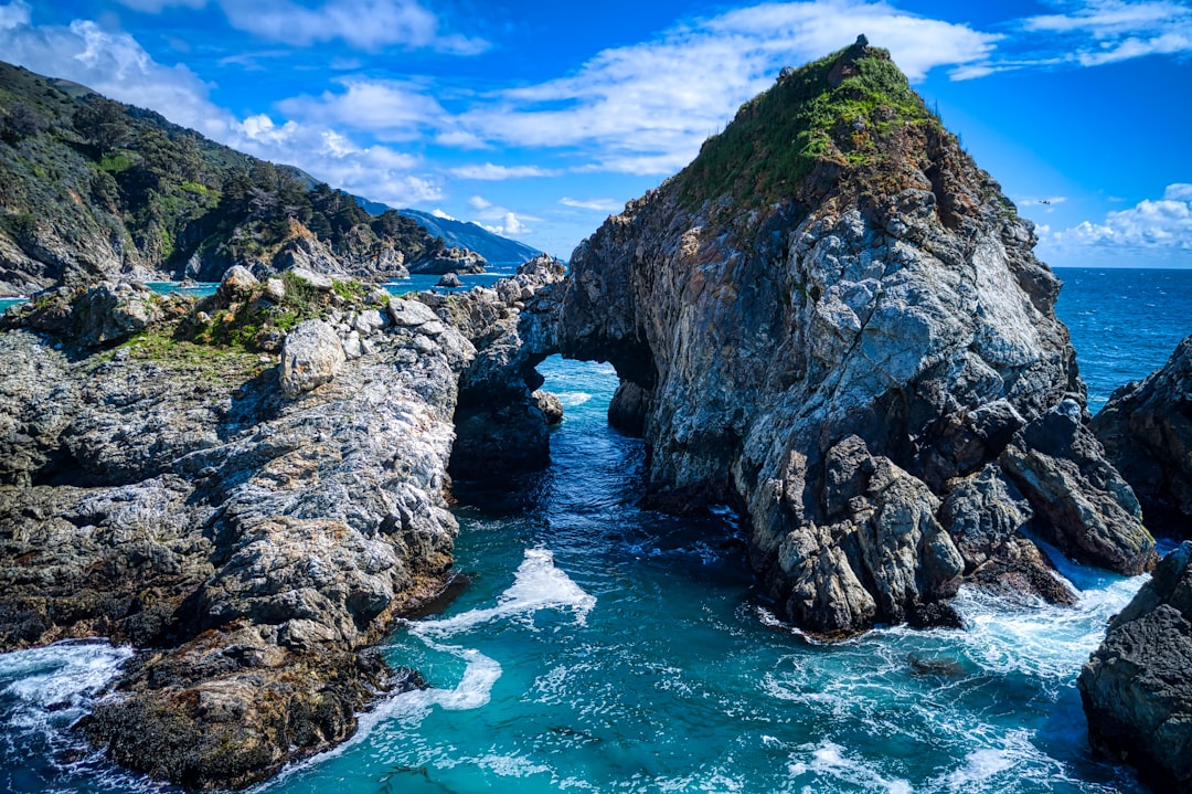 green and black rock formation beside body of water during daytime