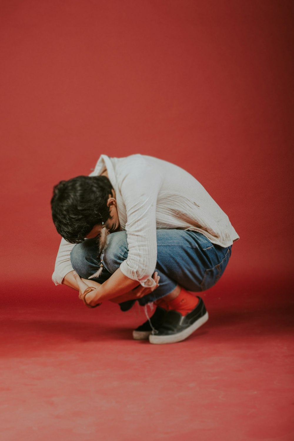 man in white long sleeve shirt and blue denim jeans sitting on red floor