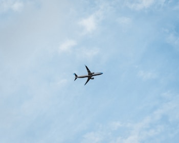 A commercial airplane is flying through a clear blue sky, offering a sense of movement and travel. The plane is seen from below, silhouetted against the vastness of the sky with subtle cloud patterns.
