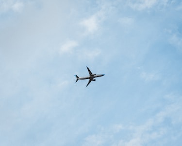 A commercial airplane is flying through a clear blue sky, offering a sense of movement and travel. The plane is seen from below, silhouetted against the vastness of the sky with subtle cloud patterns.