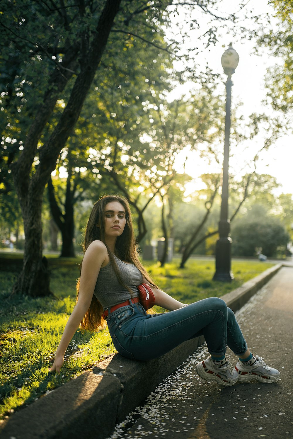 femme en jean bleu assis sur un chemin en béton pendant la journée