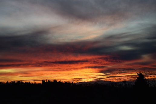 A dramatic Sicilian landscape at dusk with deep red skies over ancient stone buildings.