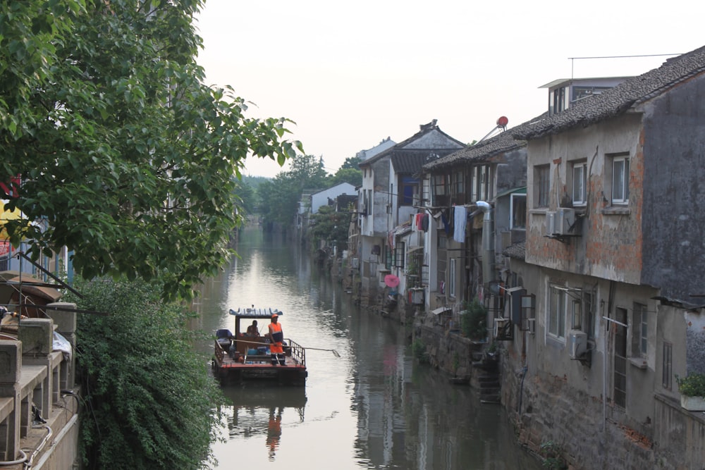 people riding boat on river between buildings during daytime