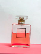Minimalist perfume bottle with soft pink liquid, placed on a marble surface with rose petals scattered around.
