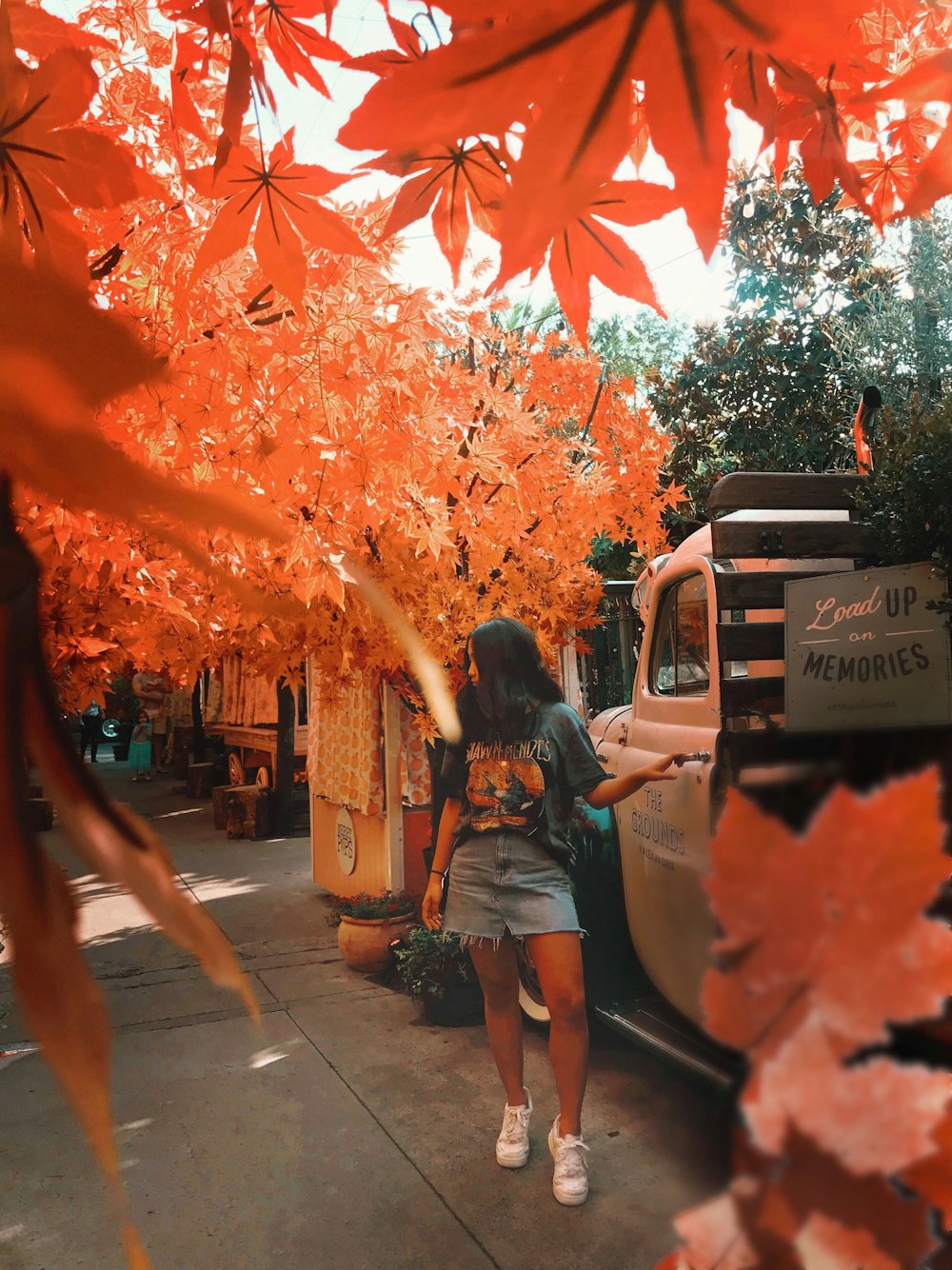 woman in blue denim shorts standing on sidewalk with red leaves during daytime