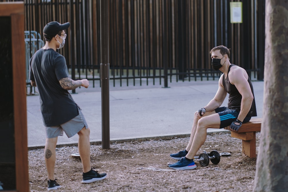 man in black t-shirt and blue shorts sitting on brown wooden pole during daytime