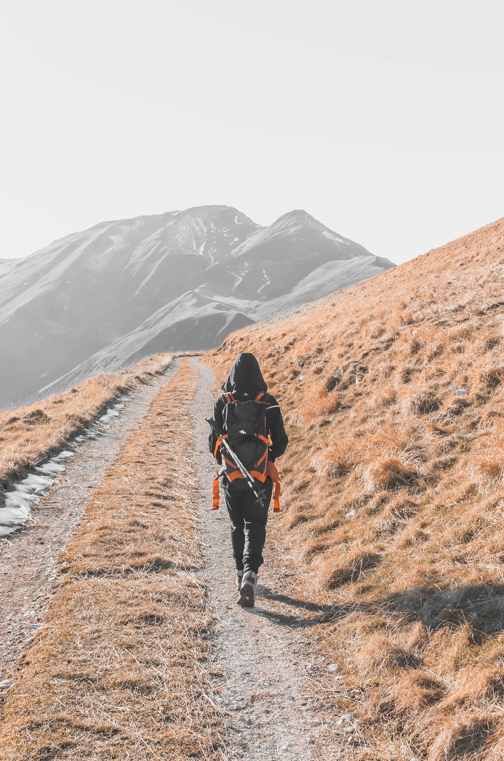 person in black jacket and black pants walking on brown dirt road during daytime