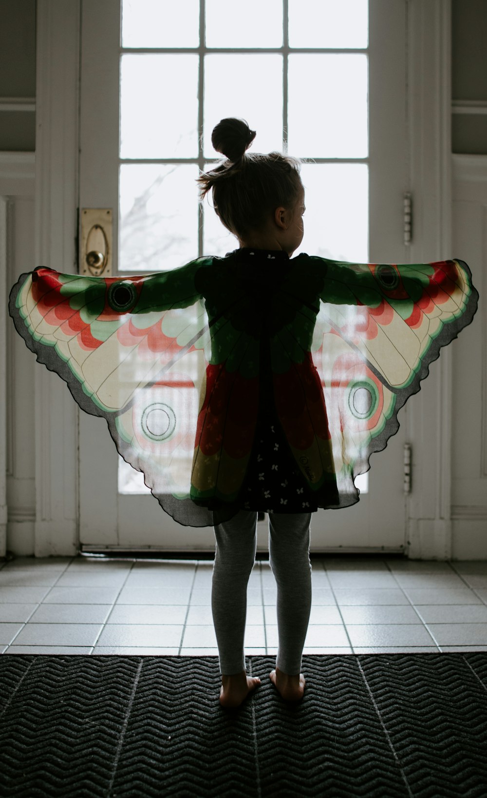 girl in black and red plaid jacket standing on white floor tiles