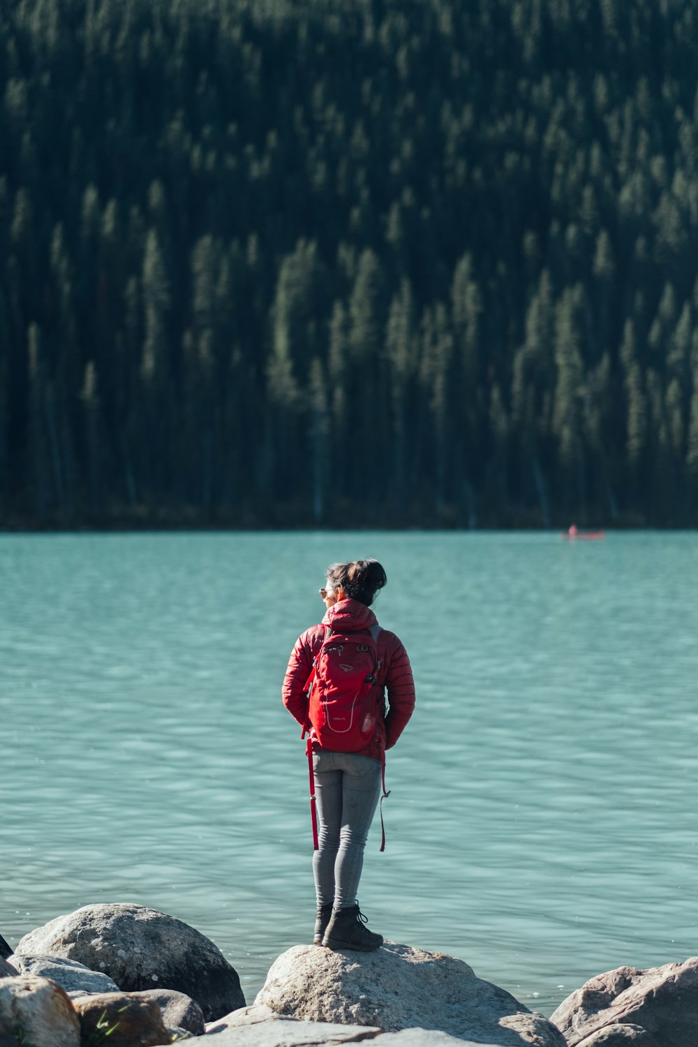 man in red jacket and gray pants standing on gray rock near body of water during