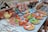 A display of colorful ceramic items and traditional souvenirs on a table. There are decorative plates with desert scenes, small pots with camel patterns, and miniature figurines of camels and people in vibrant attire. There are also crafted necklaces with beads and charms laid out to one side.