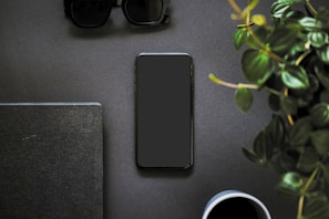 A flat lay of a notebook, pen, and a smartphone showing a course interface, surrounded by fresh leaves and a soft beige fabric.