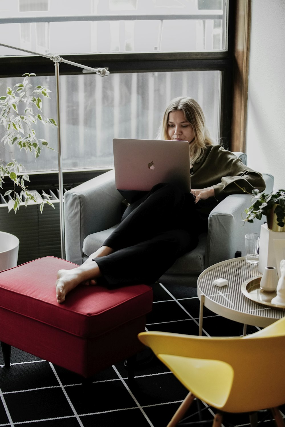 woman in white shirt and black pants sitting on red sofa using macbook