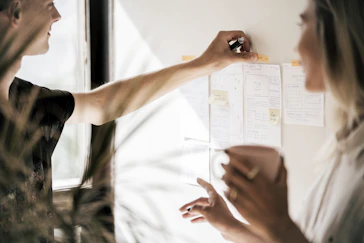 A mentor and mentee discussing strategy in a sleek modern office, with charts and notes visible.