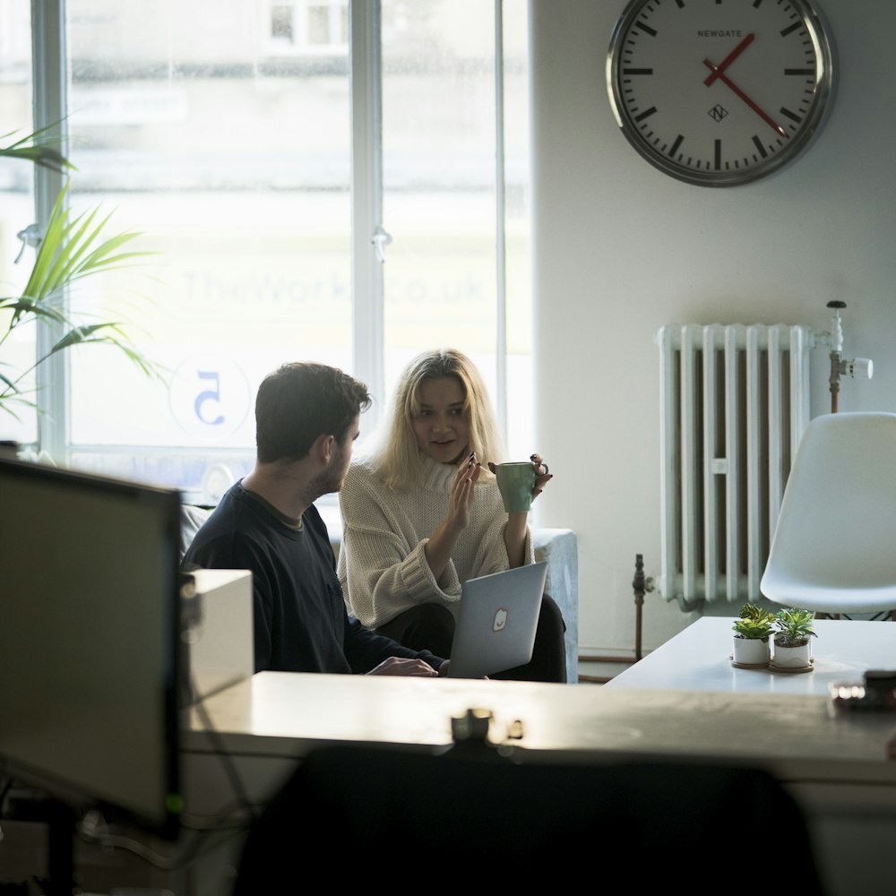 Uomo e donna che si siedono sulla sedia davanti al macbook d'argento