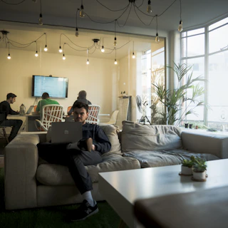 man in black t-shirt sitting on couch using macbook