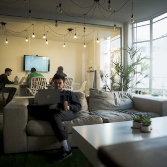 man in black t-shirt sitting on couch using macbook