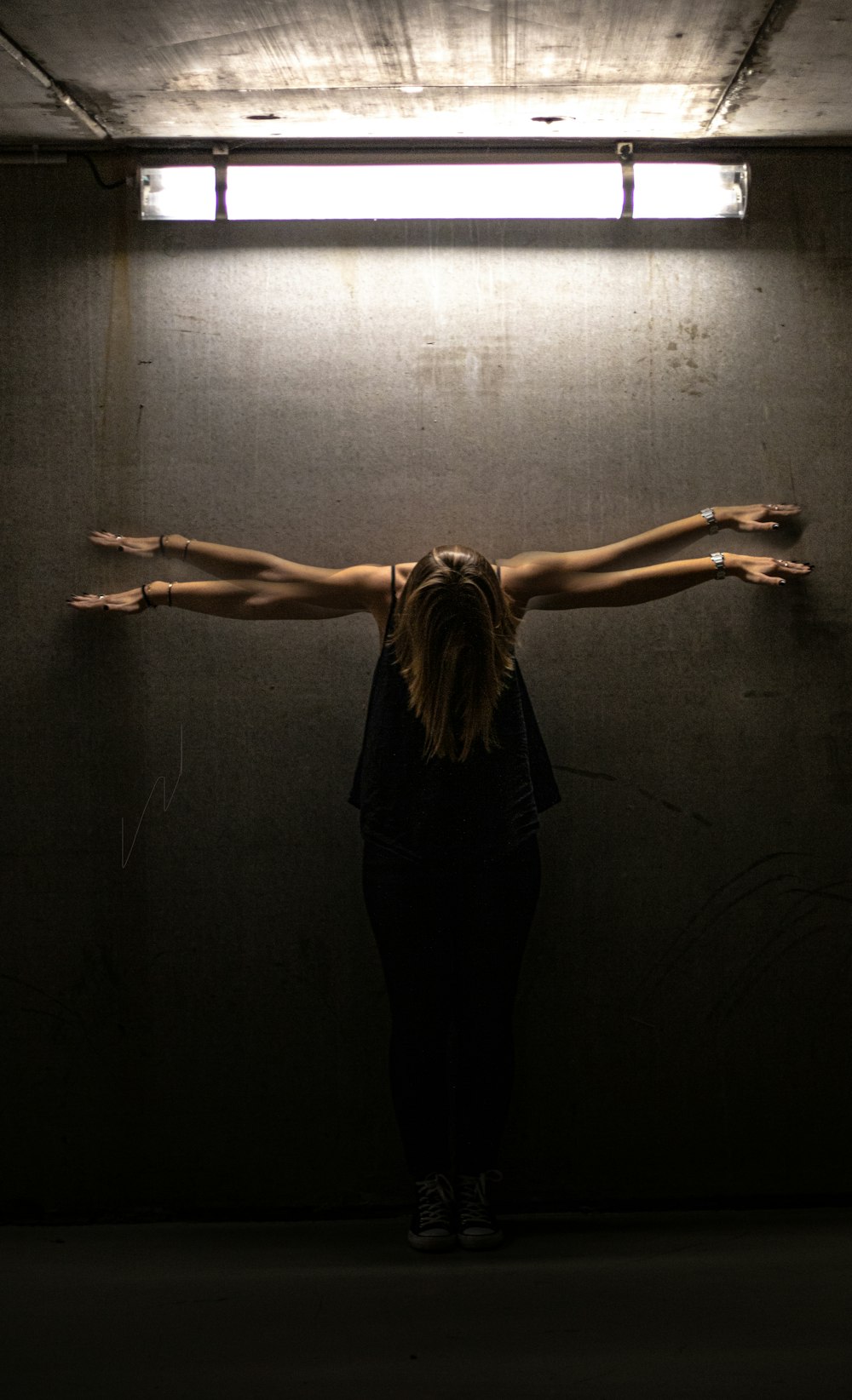 woman in black tank top and black pants standing on gray wall