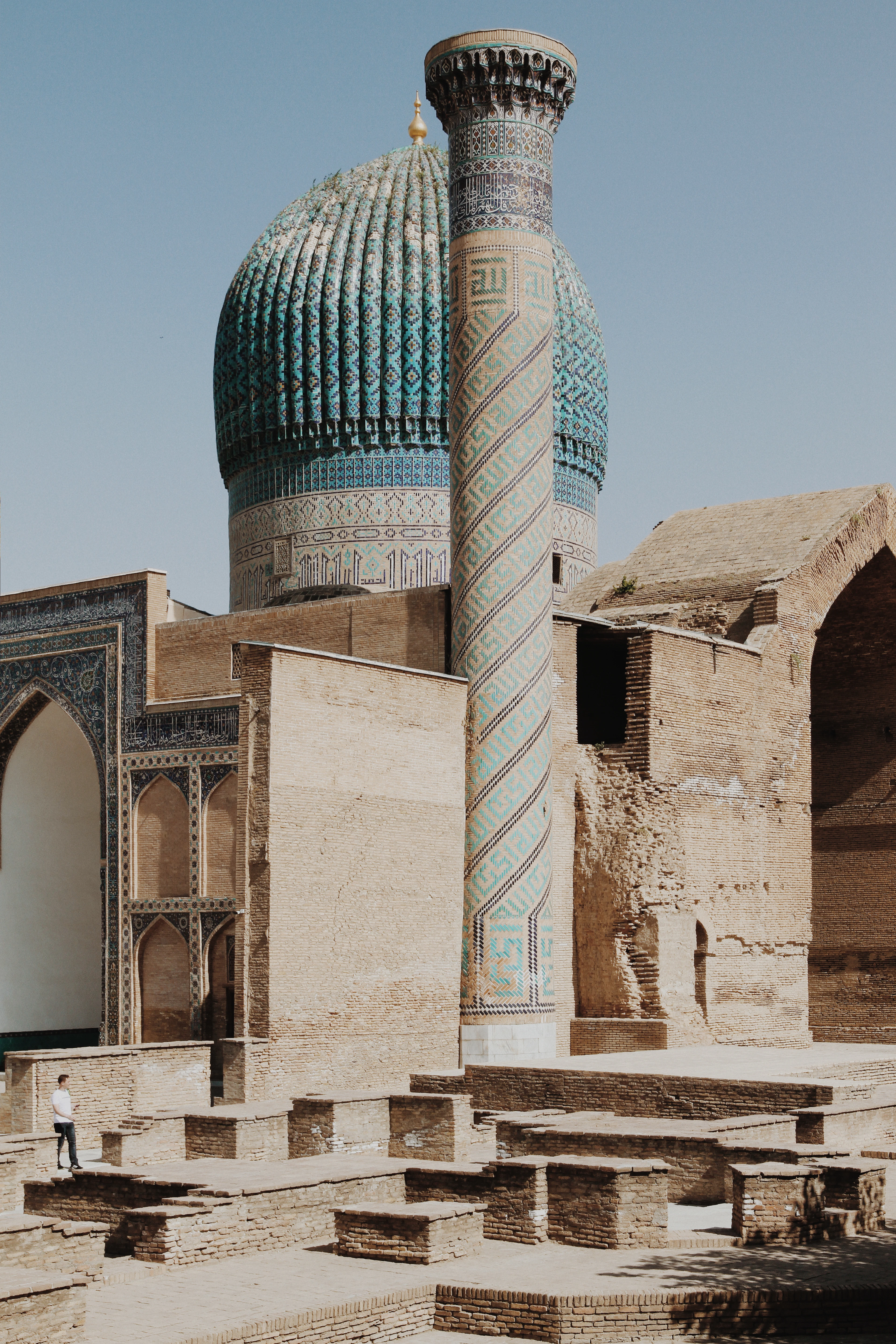 The huge ribbed turquoise dome of the Bibi-Khanym Mosque in Samarkand above bare brick walls and a spiral-tiled minaret
