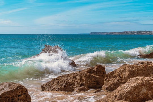 brown rock formation near sea waves during daytime in Lagos Portugal