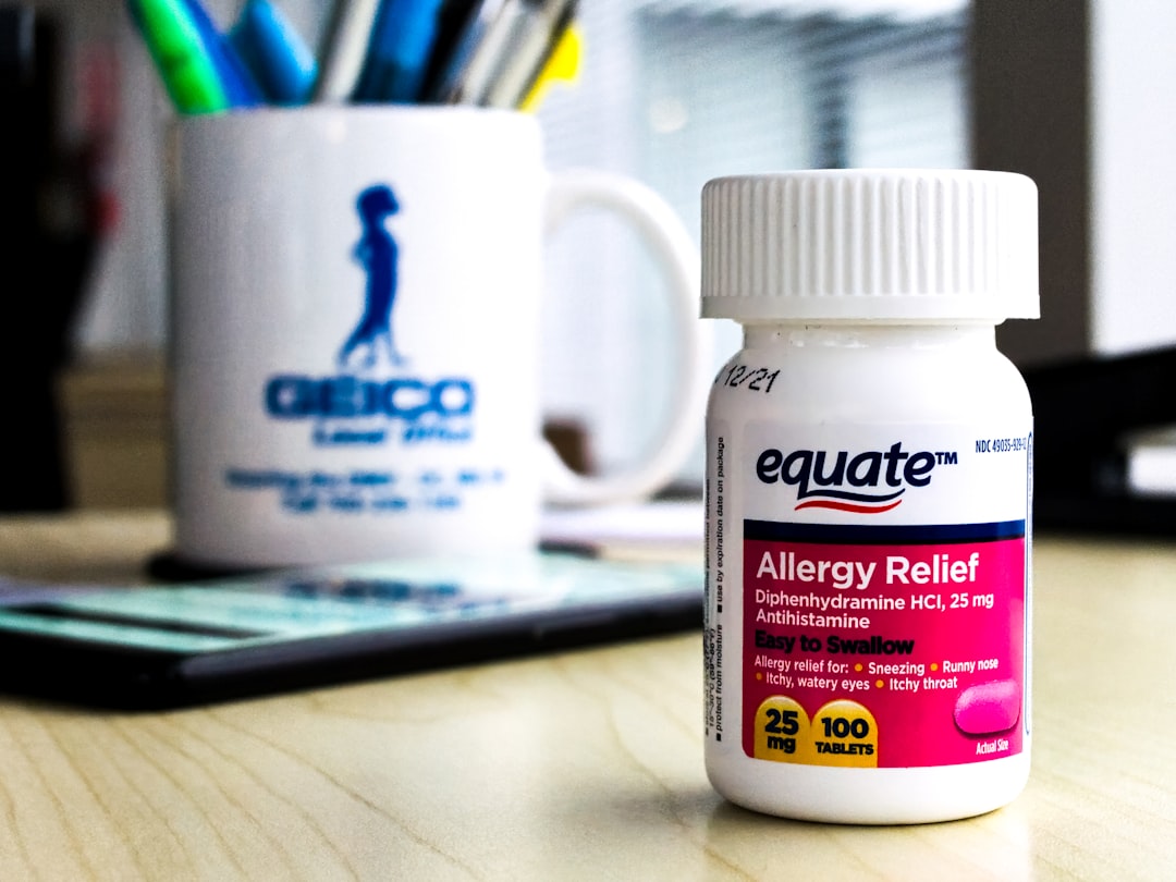 A bottle of equate brand allergy medicine on an office desk in daylight, with a Geico mug and Google Pixel 3XL in the background. 