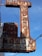 A rusted vintage sign with faintly visible words reading 'AUTO PARTS' and 'AUTO PAINTS', accompanied by some old light fixtures and electric wiring against a clear blue sky.