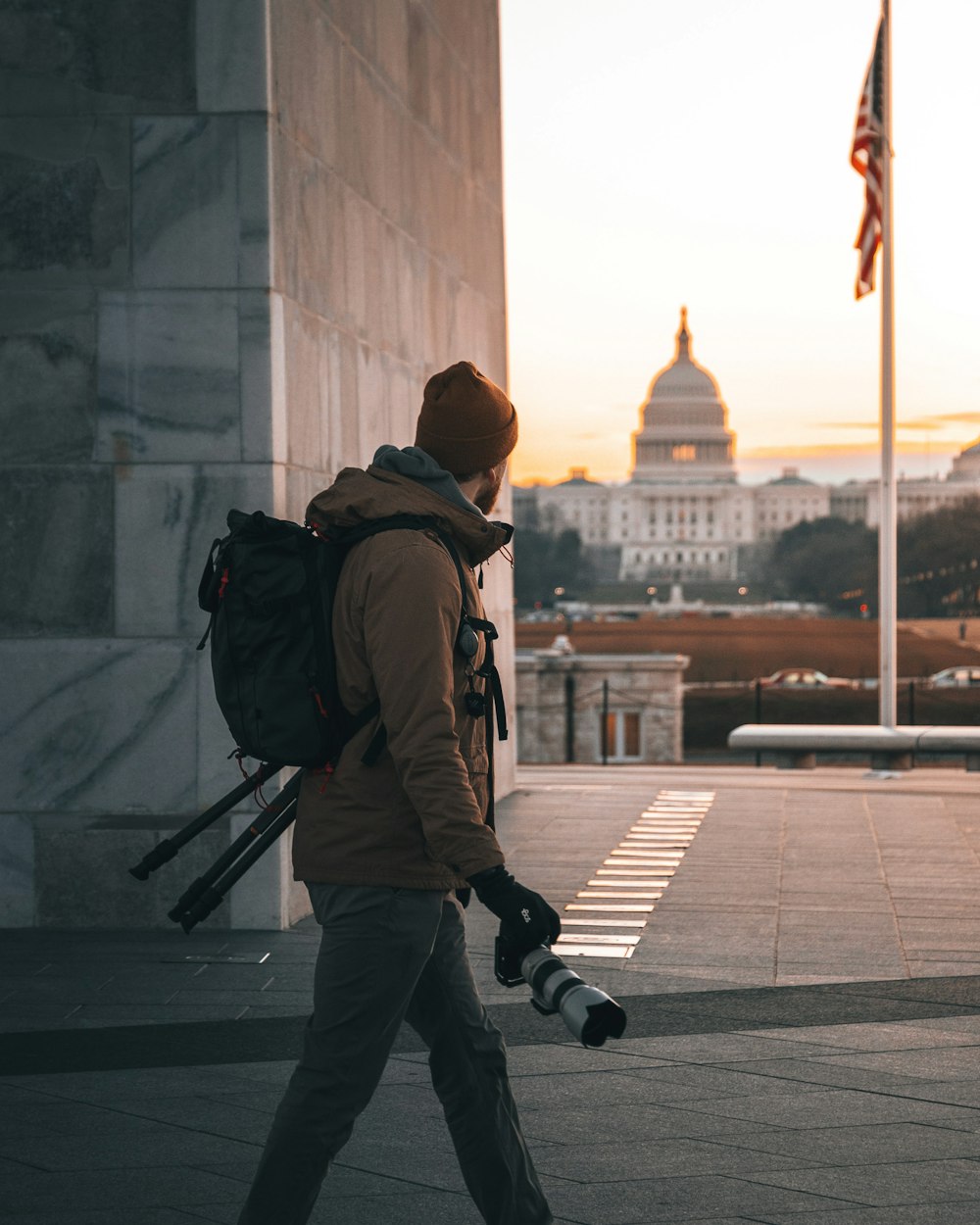 man in brown jacket and black pants wearing brown knit cap walking on sidewalk during daytime