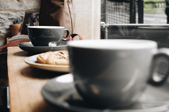 A cozy scene with a variety of colorful coffee cups and tumblers arranged on a wooden table near a window.