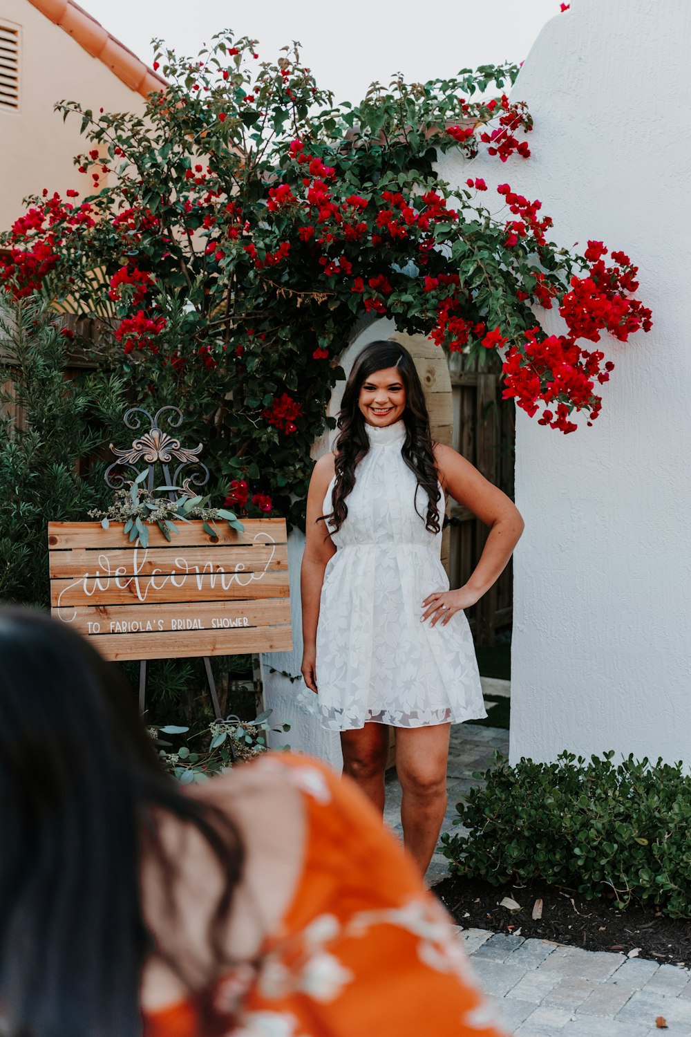 woman in white sleeveless dress standing beside red flowers