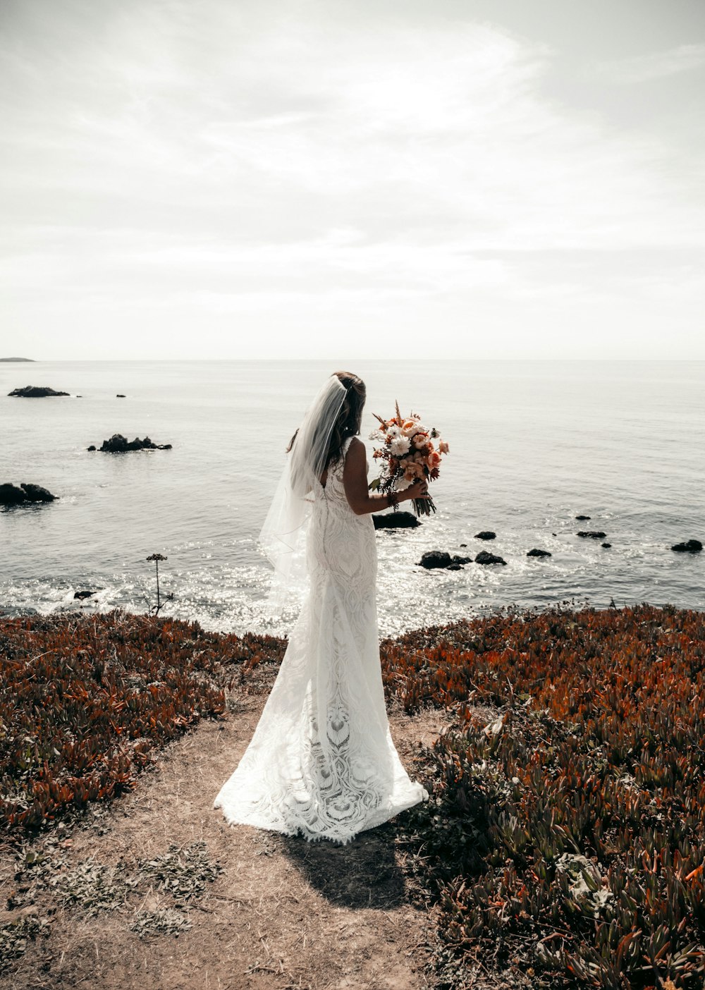 낮 동안 바위 해안에 서 있는 하얀 웨딩 드레스를 입은 여자