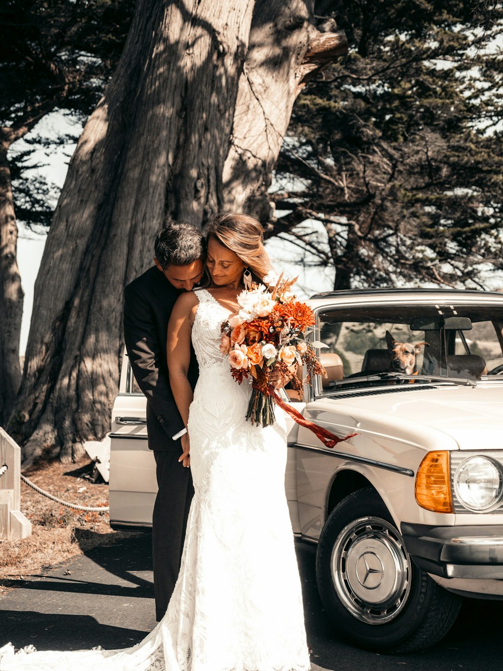 woman in white wedding gown holding bouquet of flowers standing beside white car during daytime