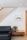 A modern living room wall with wooden vertical slats running diagonally, complemented by a black sofa on the left. A small wooden side table holds a potted plant and books. A framed artwork of birds is on the wall above the sofa.