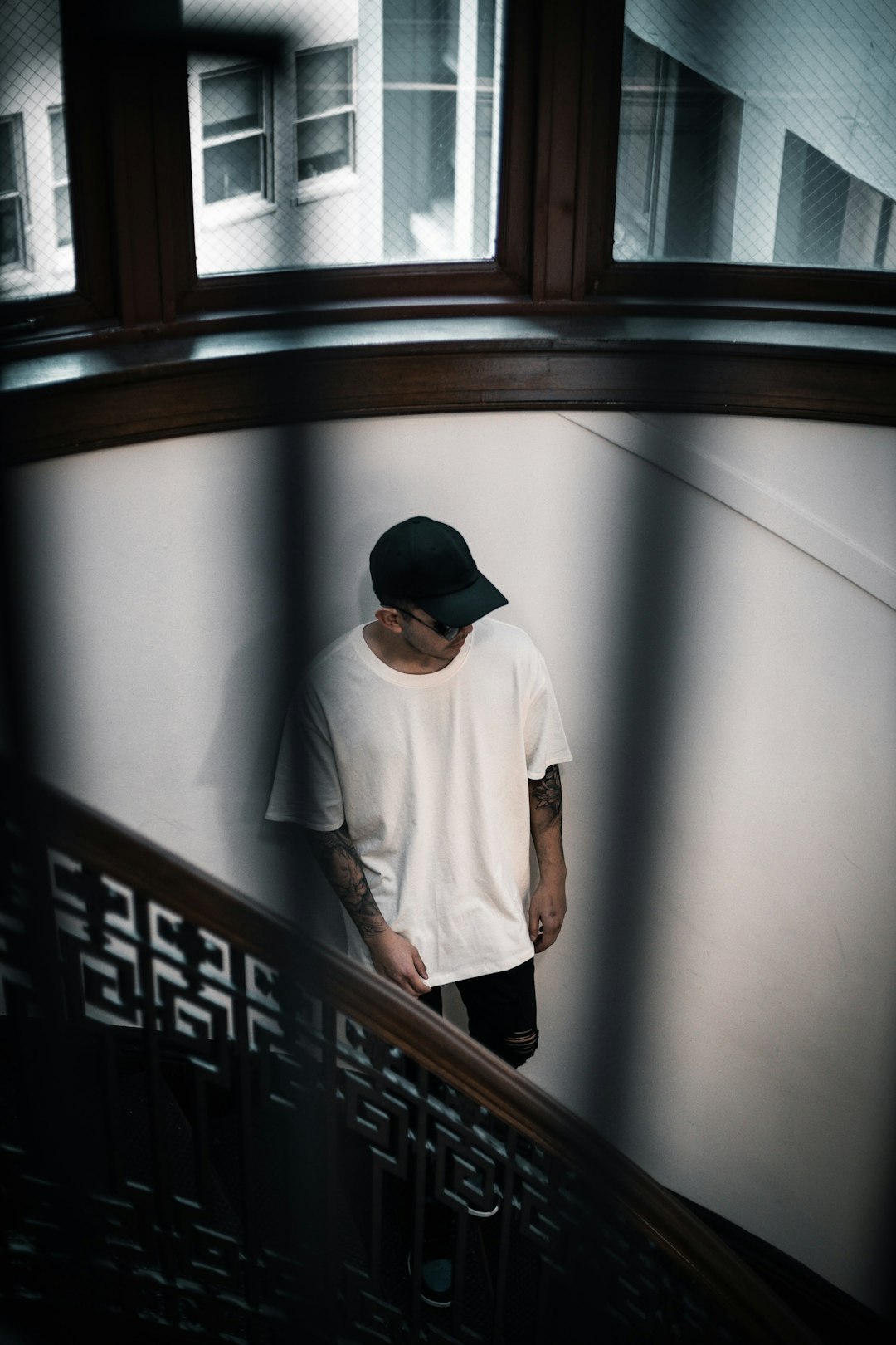 man in white long sleeve shirt and black cap standing beside brown wooden window