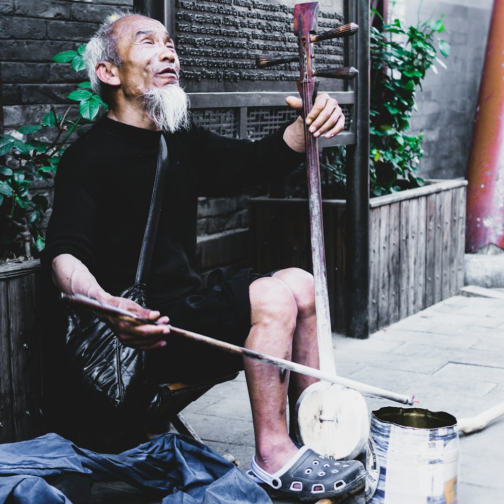 man in black long sleeve shirt holding stick sitting on concrete floor